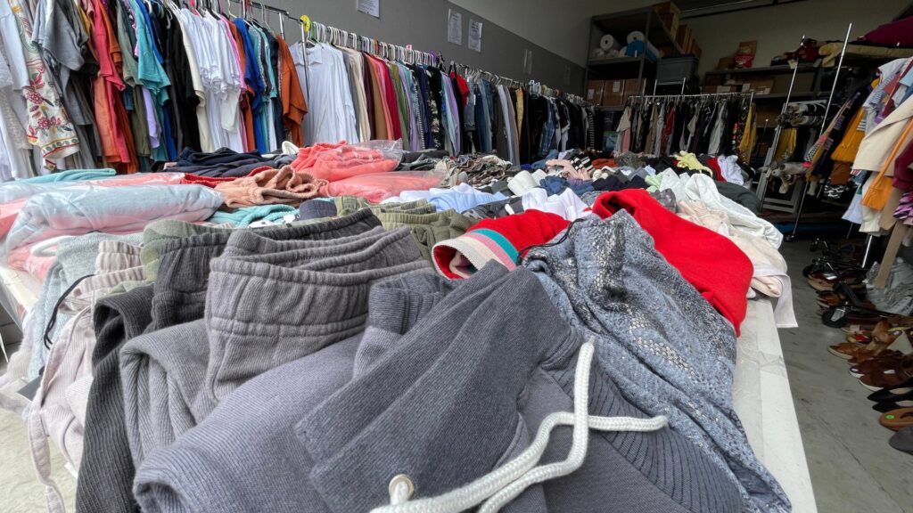 Photo of pants stacked on tables and shirts hung up on clothing racks.